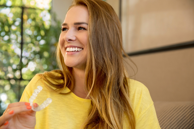 Eine glückliche Patientin hält einen Invisalign Aligner in der Hand
